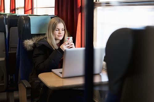 Tyttö istuu junassa ja selaa kännykkää