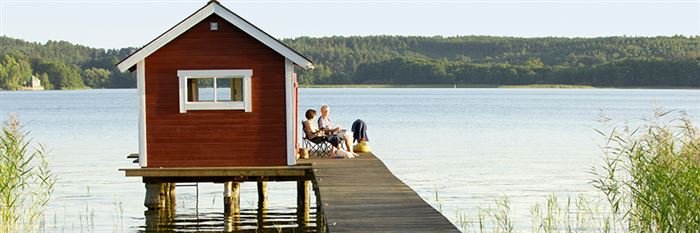 Pariskunta istuu aurinkotuoleissa pitkän laiturin päässä uimamökin edustalla.