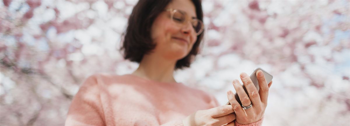 Nainen tutkii puhelinta, vaaleanpunaisia kirsikkapuita taustalla