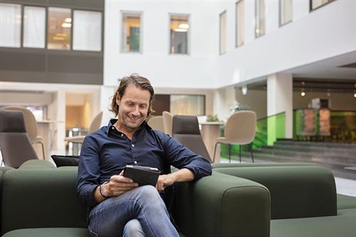 Mies selaa tablettia vihreällä sohvalla.