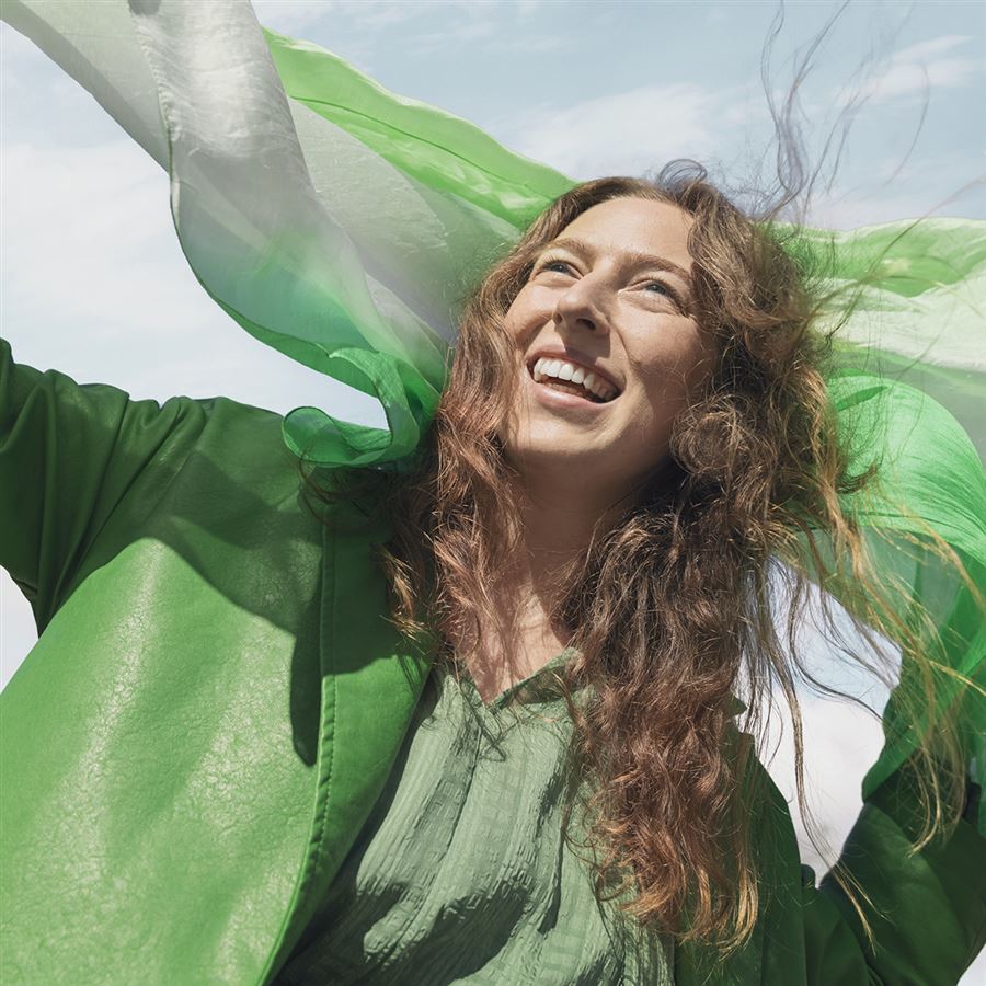 Vihreään pukeutunut nuori nainen hymyilee tuulessa