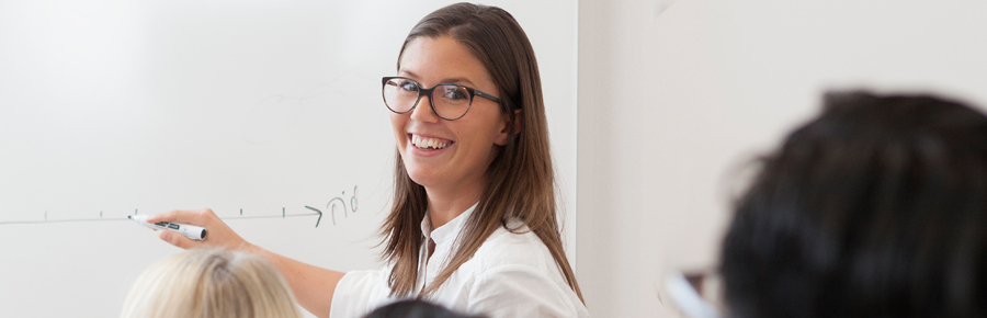 a woman drawing numbers on a whiteboard in front of people