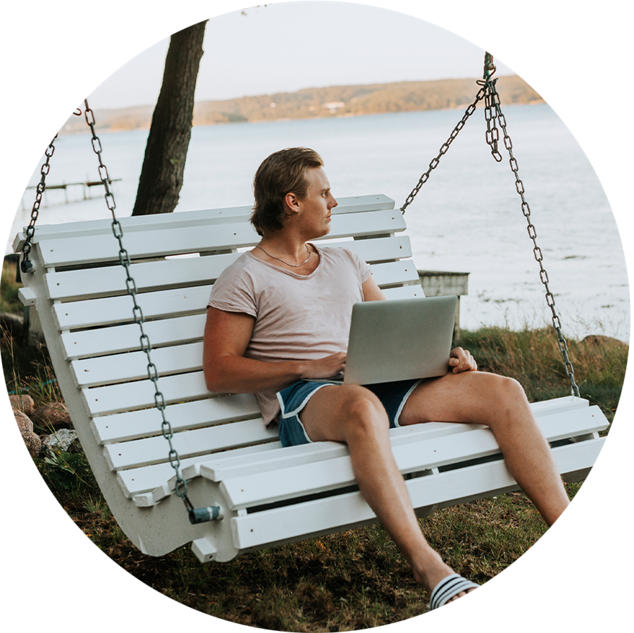 En ung man sitter på en gunga på stranden med en bärbar dator i knät.