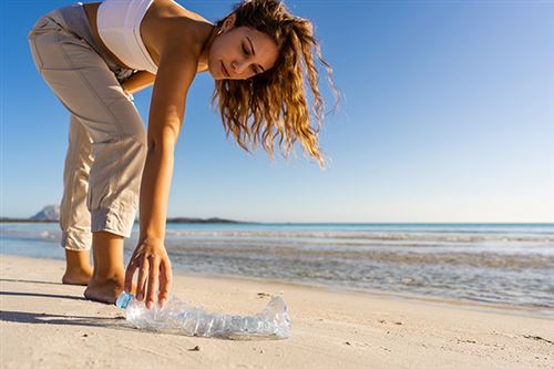 Nainen poimii muovipullon hiekkarannalta.