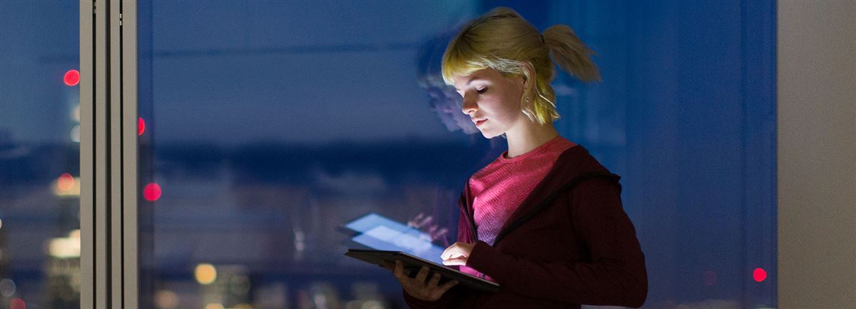 En kvinna som står och tittar ner på sin iPad på natten