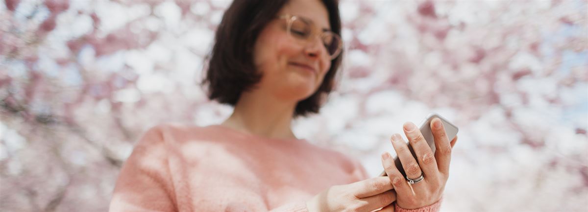 Kvinnan tittar på telefonen, med rosa körsbärsträd i bakgrunden