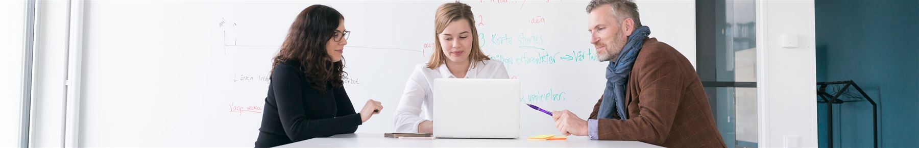 Tre personer sitter och tittar på en bildskärm med en whiteboard i bakgrunden.