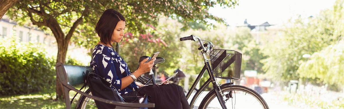 Kvinna sitter på en parkbänk med cykeln bredvid sig.