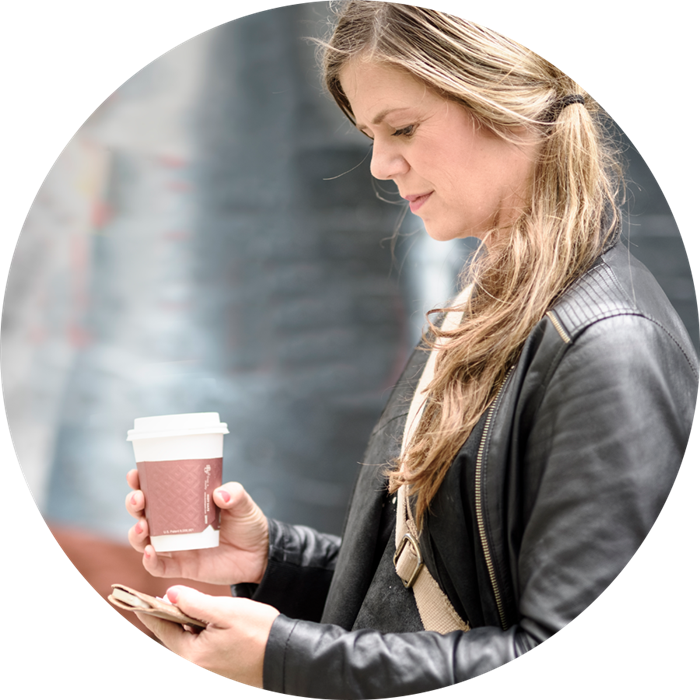 En kvinna med en kaffemugg i ena handen och en telefon i den andra.