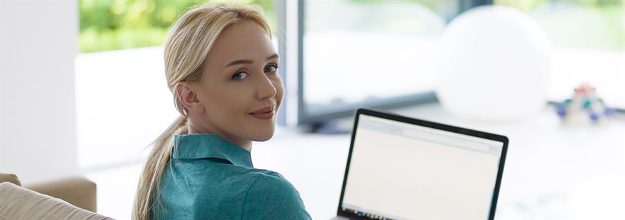 En kvinna tittar bakåt över axeln, med en bärbar dator framför sig.